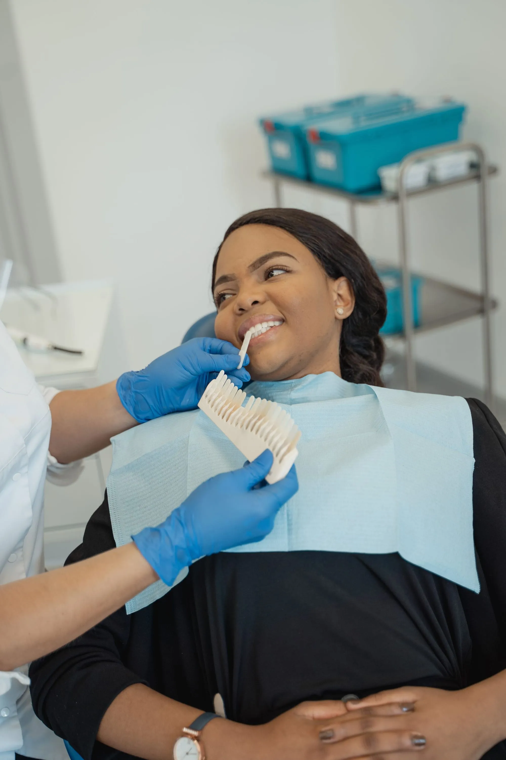Paciente sonriendo mientras la dentista compara el color de sus dientes con una guía de tonos